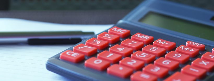 Kalkulator z czerwonymi klawiszami i długopis na dokumentach finansowych z wykresem w tle