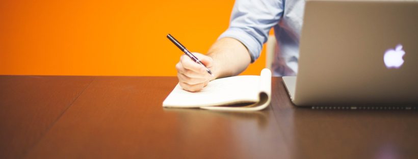 Mężczyzna przy biurku notujący coś obok laptopa, prowadząc działalność gospodarczą
